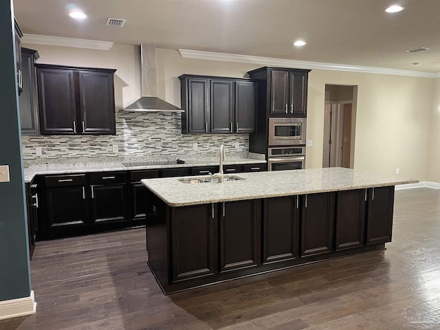 kitchen with wall chimney exhaust hood, sink, tasteful backsplash, an island with sink, and stainless steel appliances