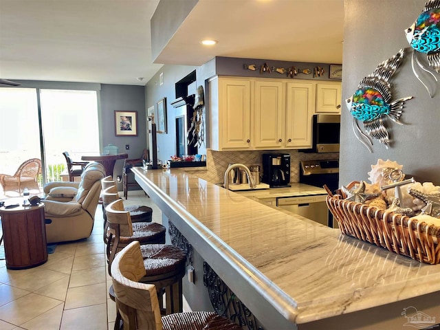 kitchen featuring appliances with stainless steel finishes, light tile patterned flooring, backsplash, kitchen peninsula, and a kitchen breakfast bar