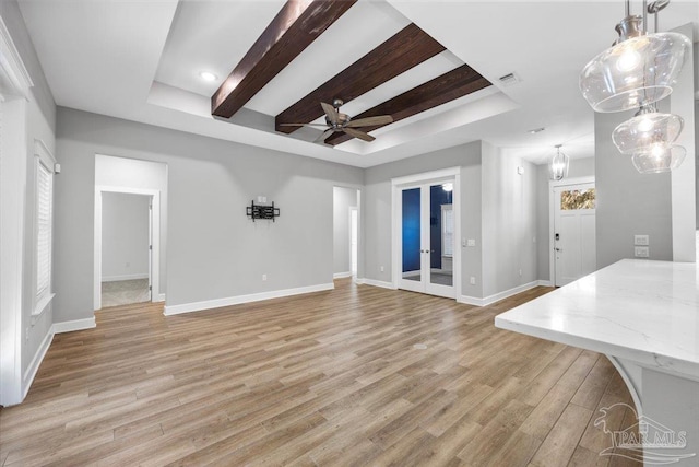 unfurnished living room featuring a raised ceiling, ceiling fan, french doors, and light hardwood / wood-style floors