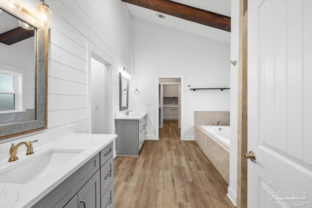 bathroom featuring tiled tub, vanity, lofted ceiling with beams, and hardwood / wood-style flooring