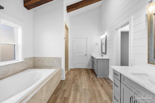 bathroom featuring tiled bath, vanity, lofted ceiling with beams, and wood-type flooring