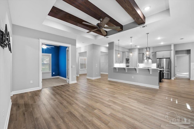 unfurnished living room featuring beamed ceiling, ceiling fan, a raised ceiling, and light hardwood / wood-style flooring