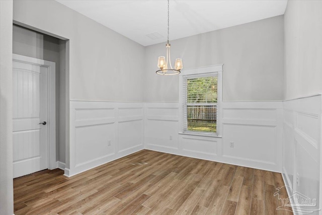 empty room with hardwood / wood-style flooring and an inviting chandelier