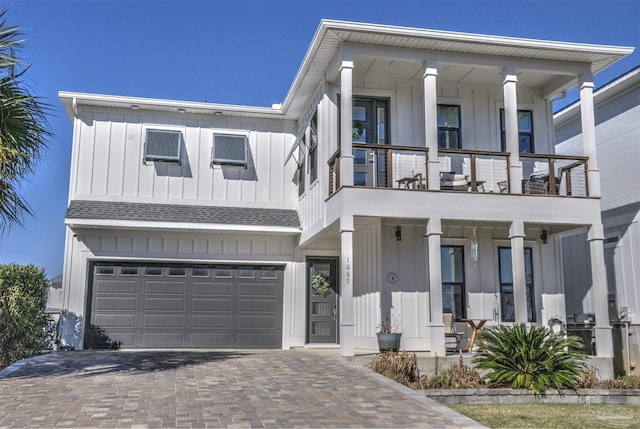 view of front of home featuring an attached garage, a balcony, roof with shingles, decorative driveway, and board and batten siding