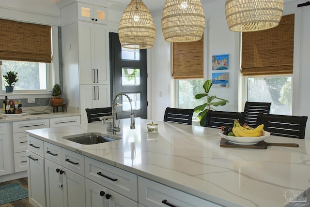 kitchen with white cabinets, glass insert cabinets, light stone countertops, pendant lighting, and a sink