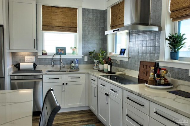 kitchen with black electric cooktop, a sink, white cabinetry, stainless steel dishwasher, and wall chimney exhaust hood