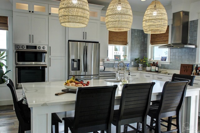 kitchen with a sink, appliances with stainless steel finishes, wall chimney range hood, backsplash, and an island with sink