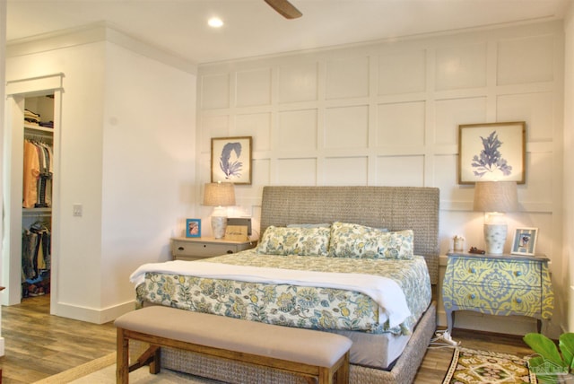 bedroom featuring a closet, a decorative wall, a spacious closet, wood finished floors, and baseboards