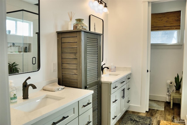 full bath featuring a stall shower, two vanities, a sink, and wood finished floors