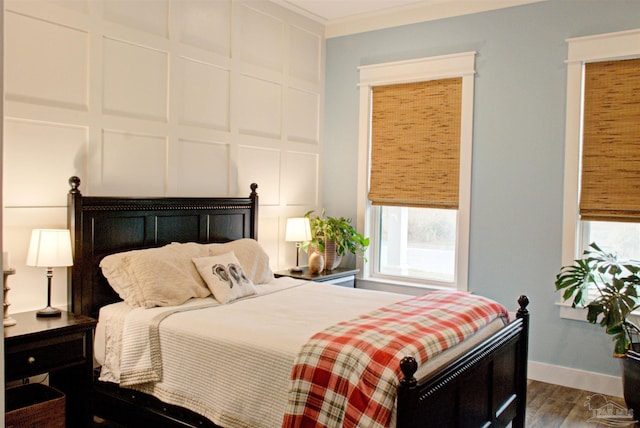 bedroom featuring crown molding, dark wood-style flooring, a decorative wall, and baseboards