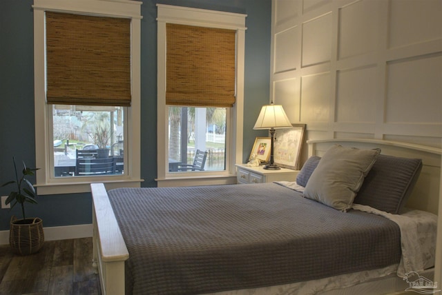 bedroom featuring baseboards, wood finished floors, and a decorative wall