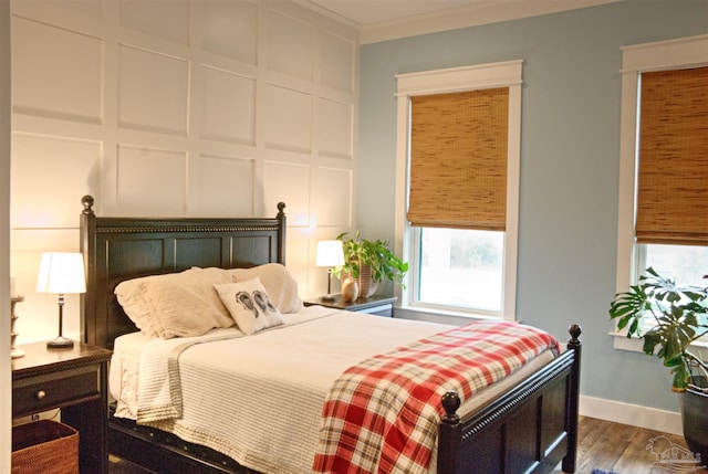 bedroom with multiple windows, ornamental molding, a decorative wall, and wood finished floors