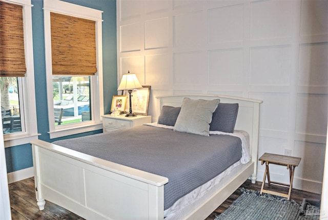 bedroom featuring baseboards, dark wood-type flooring, and a decorative wall