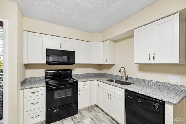 kitchen with black appliances, sink, white cabinets, and light hardwood / wood-style floors