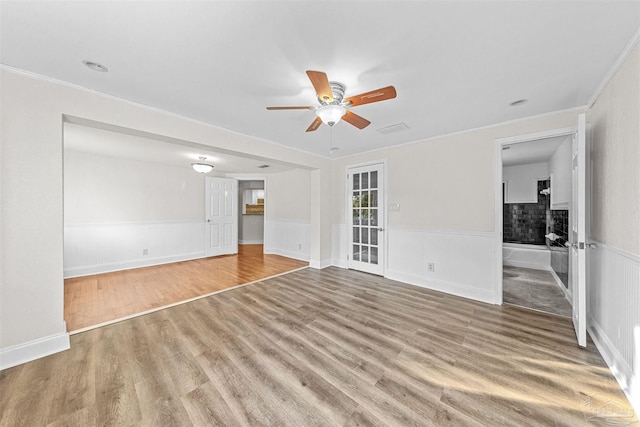 unfurnished room featuring a ceiling fan, a wainscoted wall, crown molding, and wood finished floors