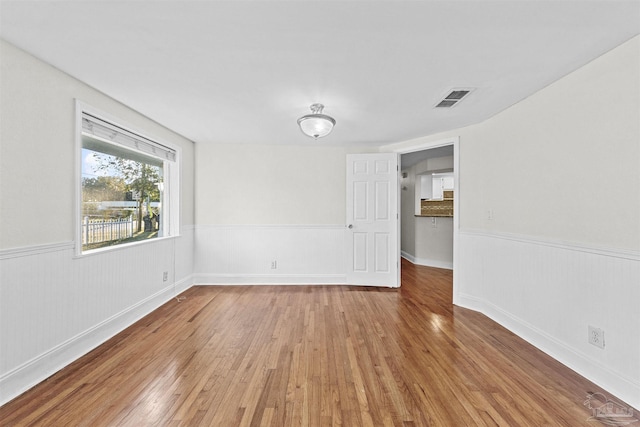 unfurnished room with a wainscoted wall, visible vents, and light wood-style floors