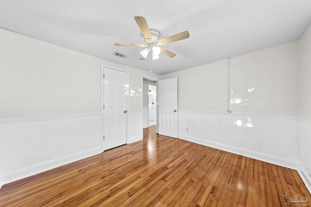 spare room with wainscoting, visible vents, ceiling fan, and wood finished floors