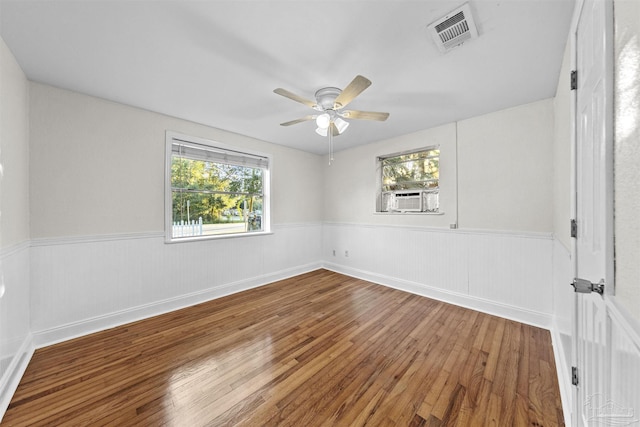 empty room featuring cooling unit, wainscoting, visible vents, and wood finished floors