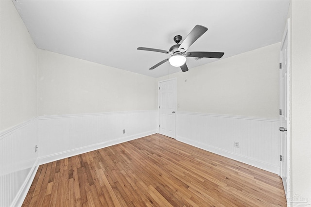 unfurnished room featuring a wainscoted wall, ceiling fan, and light wood-style floors