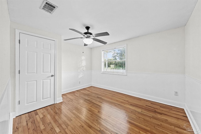 unfurnished room with a wainscoted wall, a ceiling fan, visible vents, and wood finished floors