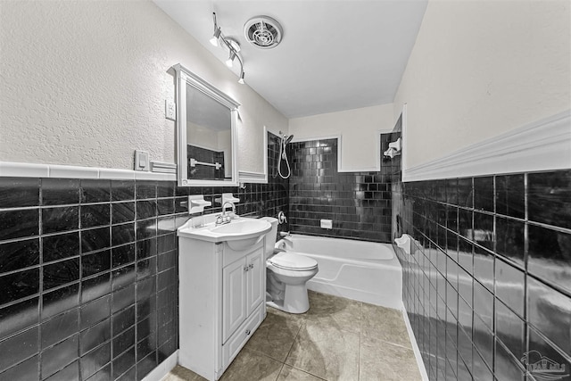 bathroom featuring wainscoting, toilet, vanity, shower / washtub combination, and tile walls