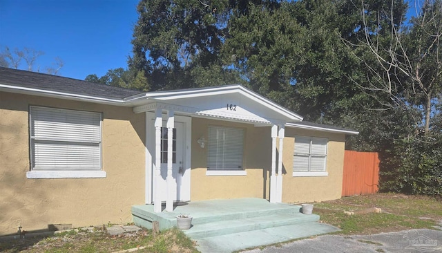 view of exterior entry featuring a shingled roof, fence, and stucco siding