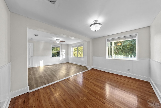 empty room featuring ceiling fan, wood finished floors, visible vents, baseboards, and wainscoting