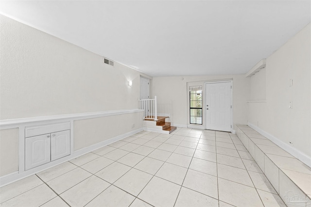 unfurnished room with light tile patterned flooring, visible vents, and stairs