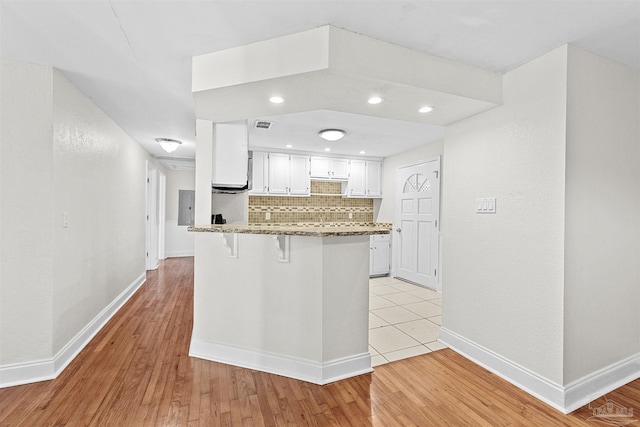 kitchen featuring a breakfast bar, decorative backsplash, stone countertops, white cabinets, and a peninsula