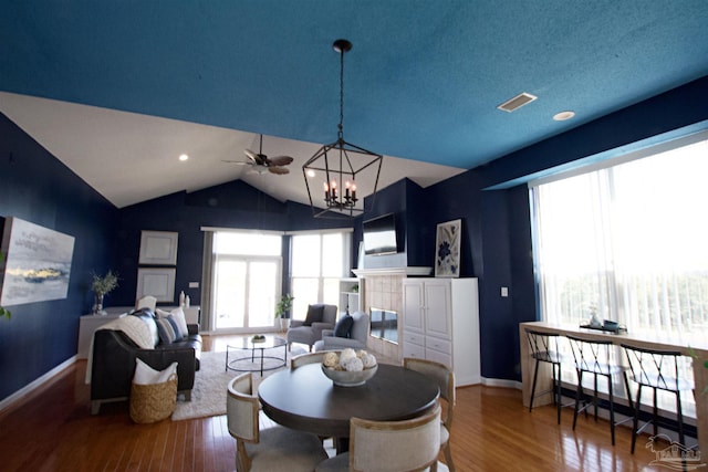 dining area with hardwood / wood-style flooring, vaulted ceiling, a fireplace, and an inviting chandelier