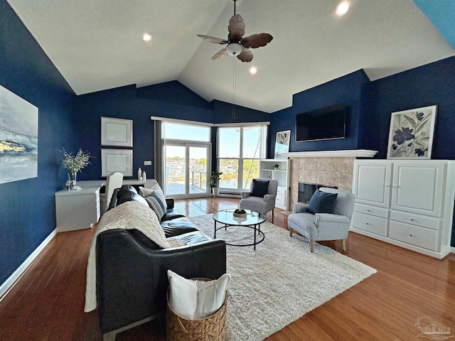 living room featuring ceiling fan, wood-type flooring, vaulted ceiling, and a tile fireplace