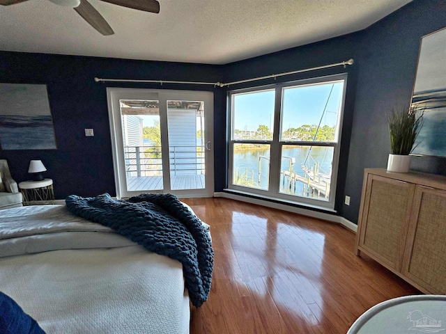 bedroom featuring ceiling fan, access to outside, a textured ceiling, light wood-type flooring, and a water view