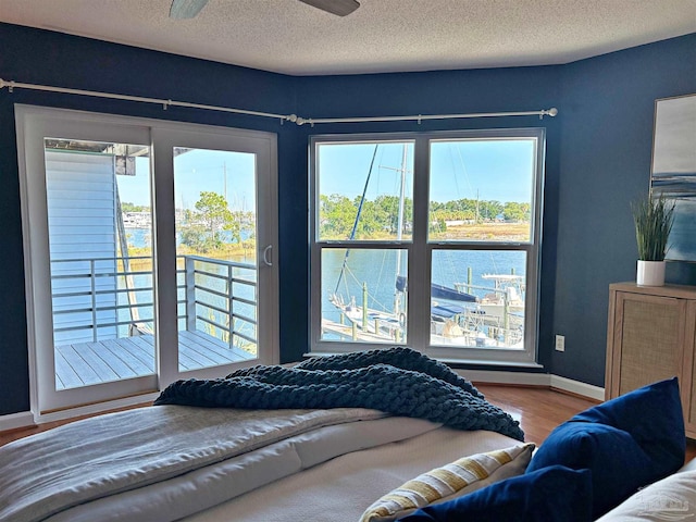 bedroom featuring a textured ceiling, access to exterior, ceiling fan, a water view, and hardwood / wood-style flooring