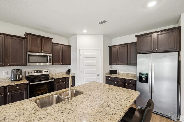 8018 Burnside Loop, Pensacola, FL 32526 - kitchen with appliances with stainless steel finishes, dark brown cabinets, light stone countertops, a kitchen bar, and recessed lighting