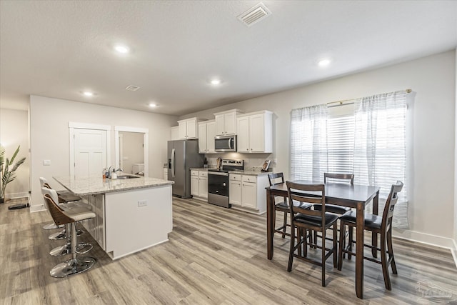 kitchen featuring a breakfast bar, white cabinetry, a kitchen island with sink, light stone countertops, and appliances with stainless steel finishes