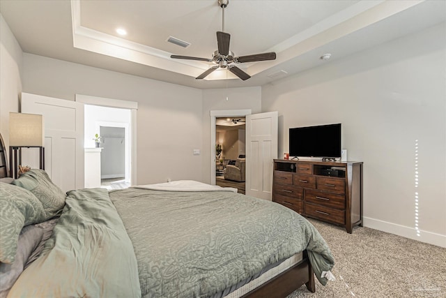 bedroom featuring a raised ceiling, ceiling fan, light carpet, and connected bathroom