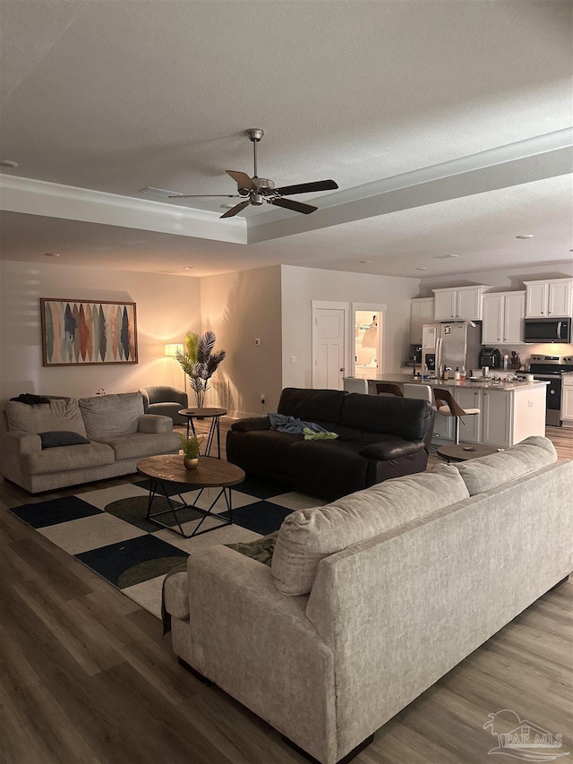 living room with ceiling fan, a tray ceiling, a textured ceiling, and hardwood / wood-style floors