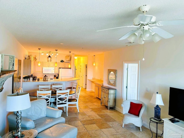 living room with a ceiling fan, stone finish flooring, a textured ceiling, and baseboards