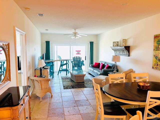 living area with visible vents, ceiling fan, and stone tile floors