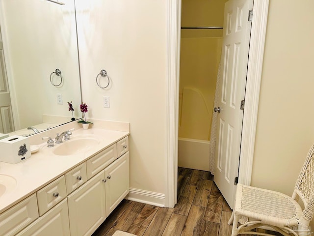 full bath featuring double vanity, wood finished floors, a sink, and baseboards