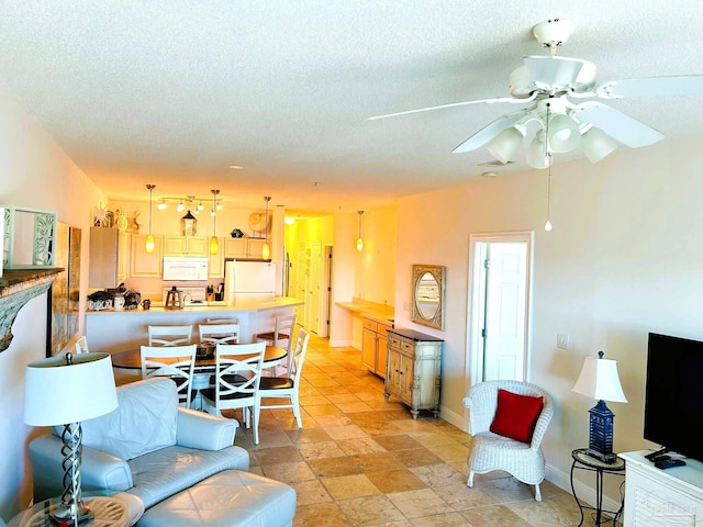 living room with a textured ceiling, ceiling fan, and baseboards