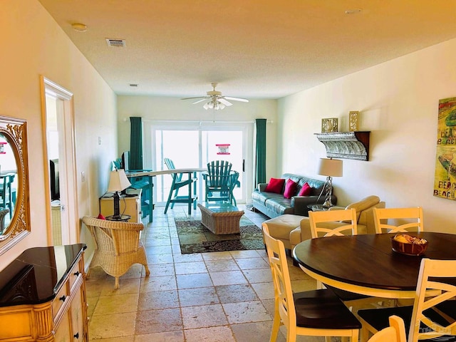 living area with a ceiling fan, stone tile flooring, and visible vents