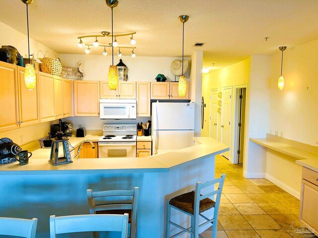 kitchen featuring white appliances, visible vents, a peninsula, hanging light fixtures, and light brown cabinets