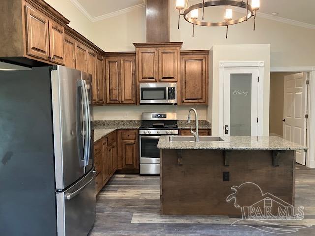 5434 Lilac Ave, Milton, FL 32570 - kitchen with stainless steel appliances, dark wood-style floors, ornamental molding, light stone counters, and a center island with sink