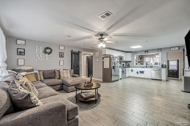 living room with ceiling fan, a barn door, and sink