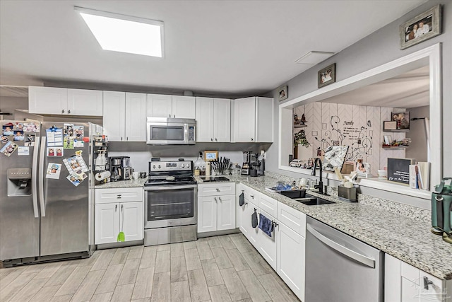 kitchen with light stone countertops, white cabinetry, appliances with stainless steel finishes, and sink