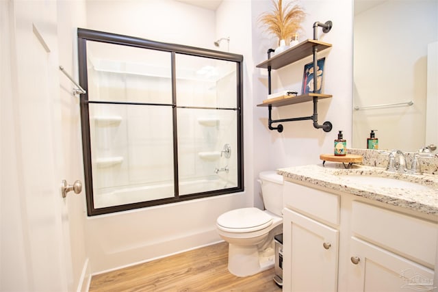 bathroom featuring toilet, vanity, wood finished floors, and bath / shower combo with glass door