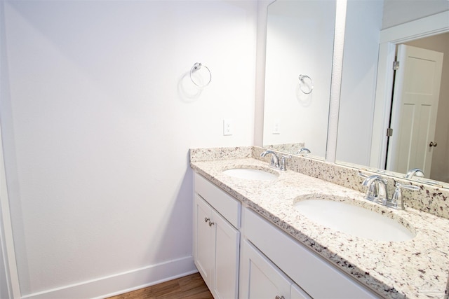 bathroom featuring wood finished floors, double vanity, a sink, and baseboards