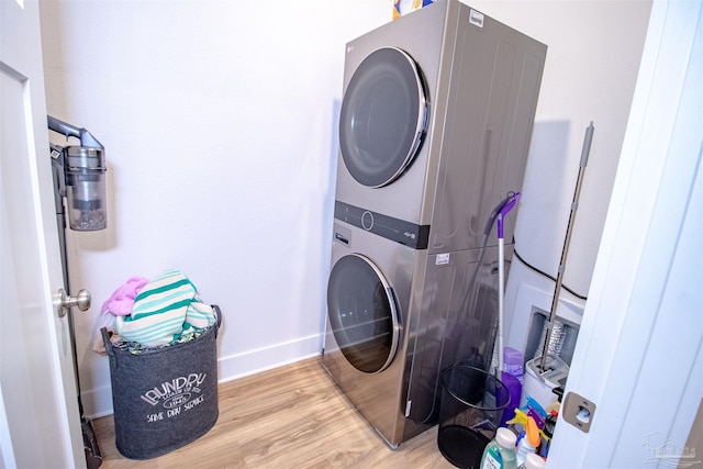 clothes washing area featuring baseboards, laundry area, wood finished floors, and stacked washer and clothes dryer