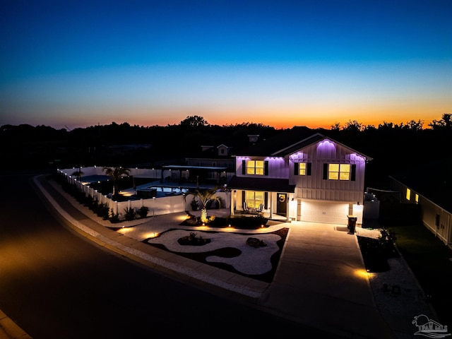 back of property at dusk with board and batten siding, fence, a garage, and concrete driveway